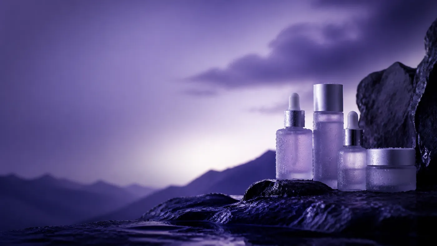 Frosted serum droppers and skincare bottles covered in dew on wet dark stone under a violet accent light