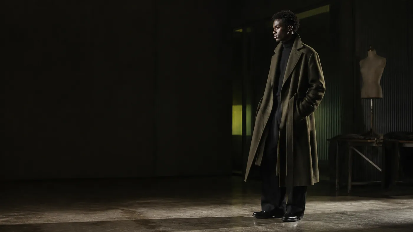 A luxury wool overcoat draped in a dark atelier under raking rim light with lime ambient glow